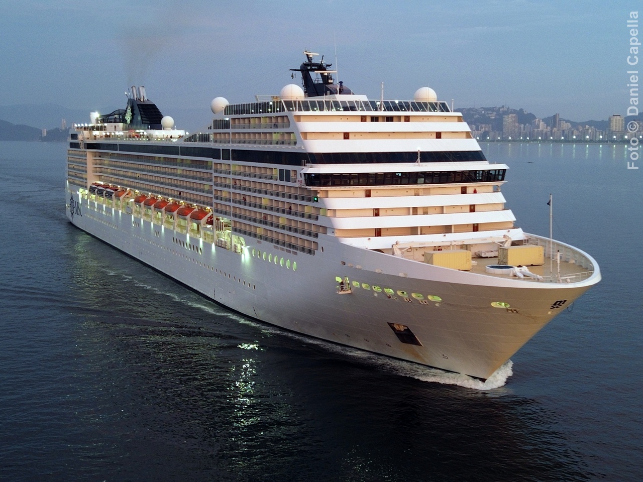 Navio MSC Musica de cor branca navegando pelo canal, visto em ângulo diagonal evidenciando sua proa e cabines com varanda