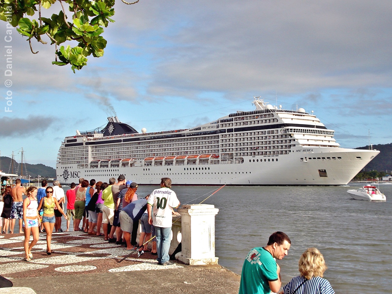 MSC Musica navegando ao fundo com passageiros observando a embarcação a partir da Ponta da Praia em Santos