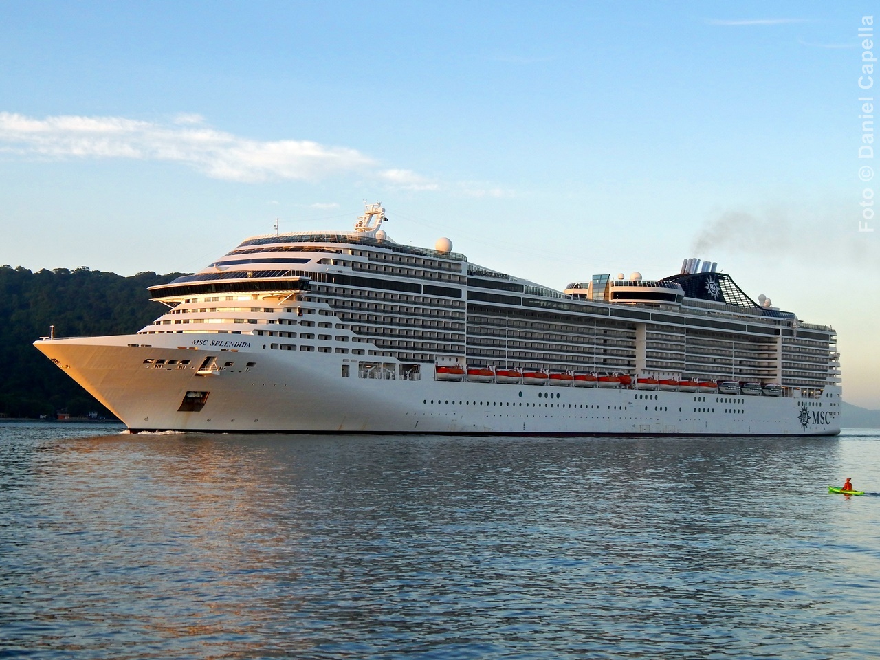 Vista lateral do navio MSC Splendida navegando em águas calmas próximo à costa iluminada pelo sol