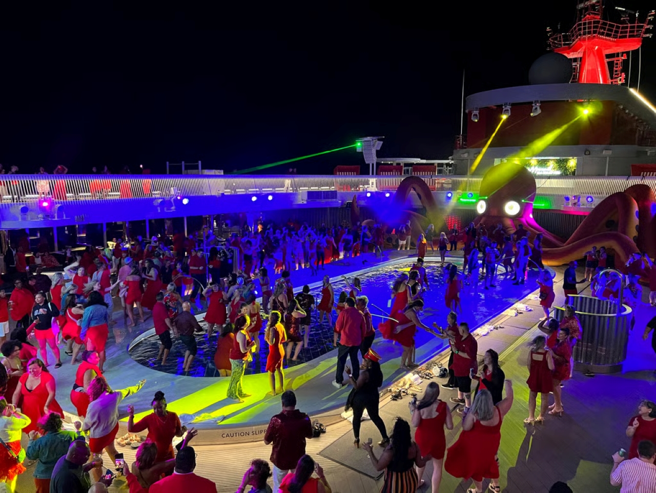 Vista de festa noturna a bordo de navio da Virgin Voyages, com luzes coloridas e piscina ao centro