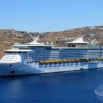Vista do Explorer of the Seas atracado no porto grego de Mykonos, com cenário árido e construções brancas ao fundo