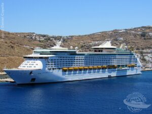 Vista do Explorer of the Seas atracado no porto grego de Mykonos, com cenário árido e construções brancas ao fundo