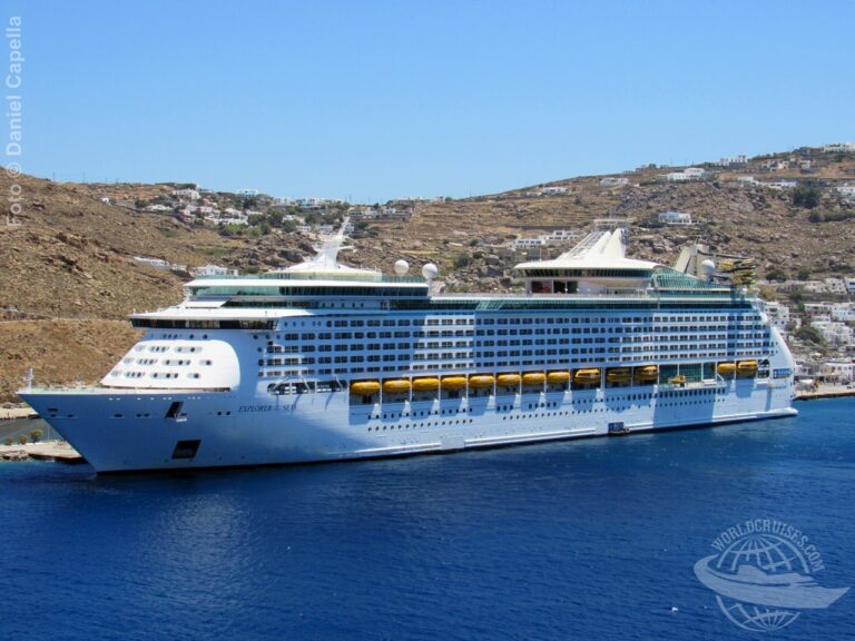 Vista do Explorer of the Seas atracado no porto grego de Mykonos, com cenário árido e construções brancas ao fundo
